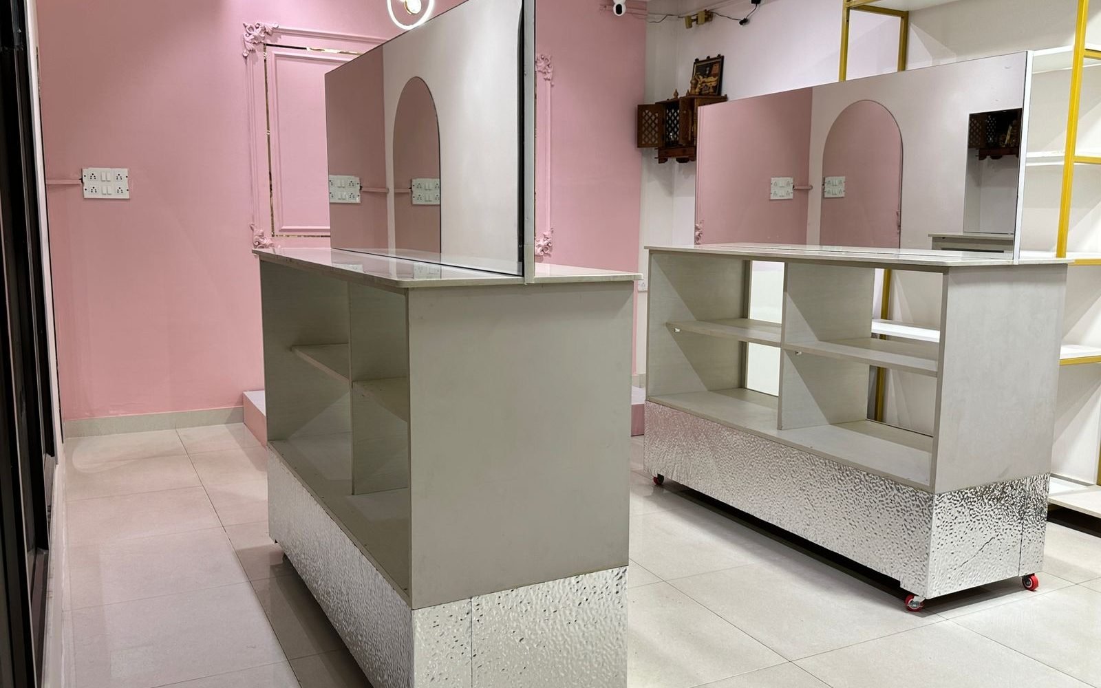 Two white display counters with mirrored upper panels and open shelving in the Ananta Designs boutique, set against the pink wall.