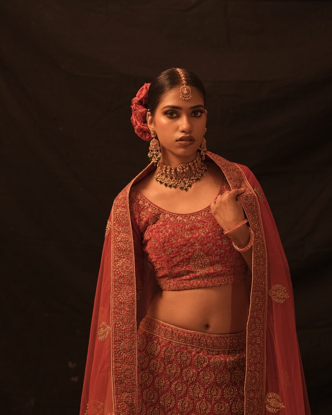 A model in a red and gold embroidered bridal lehenga with a matching dupatta.