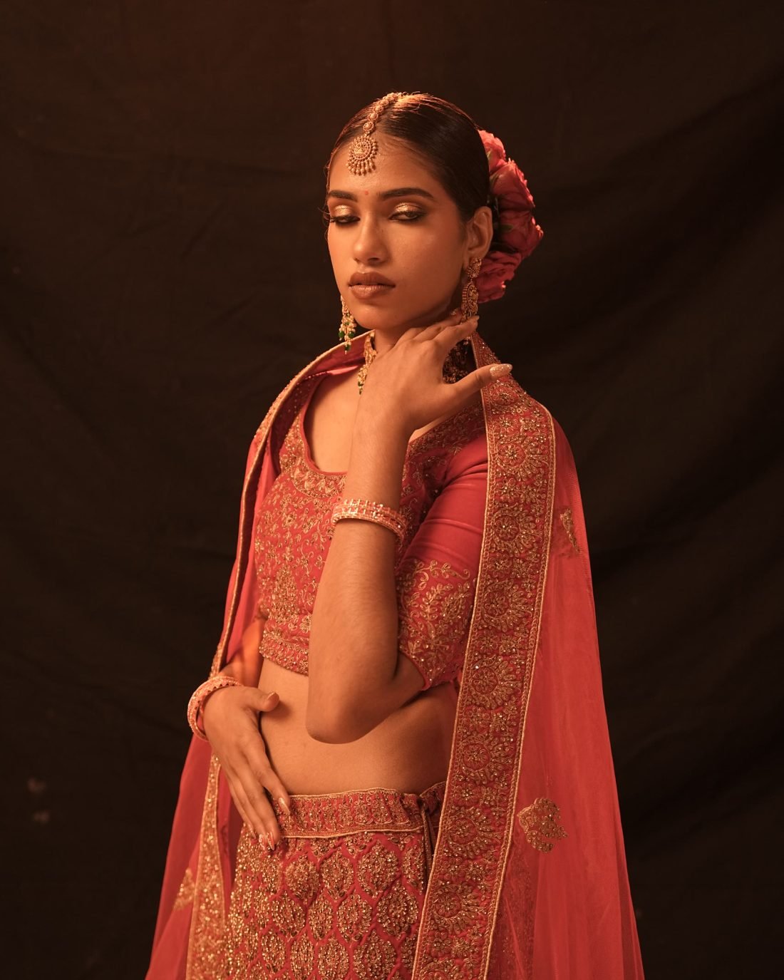 A model standing in a red and gold embroidered bridal lehenga with a draped dupatta.