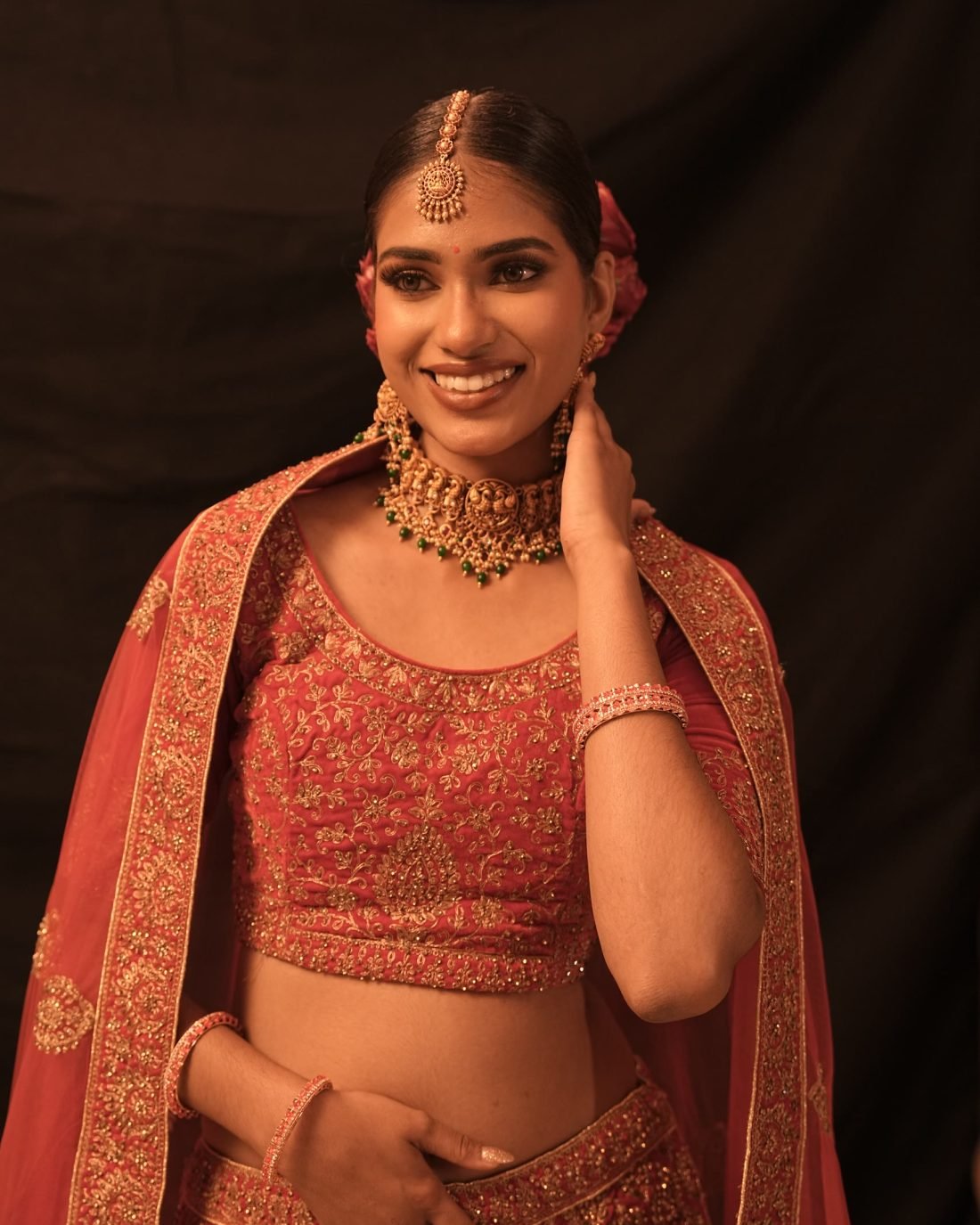 A model in red bridal dress with gold jewellery and floral hair styling.