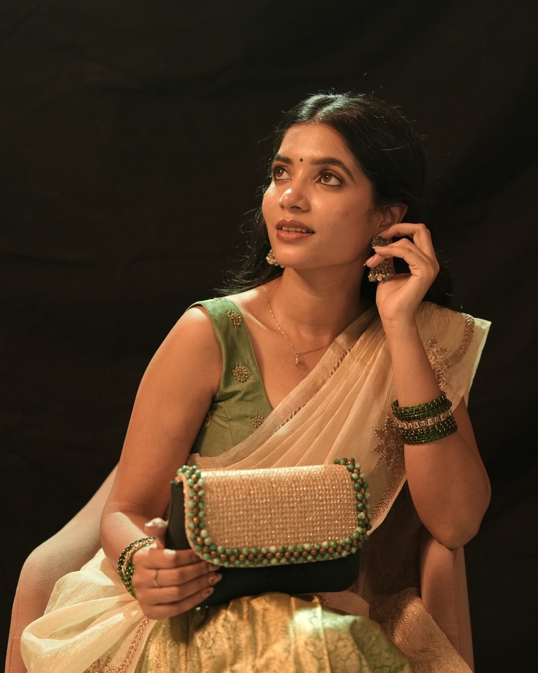 Portrait of a model in a cream and gold saree with jhumka earrings, against a dark backdrop.