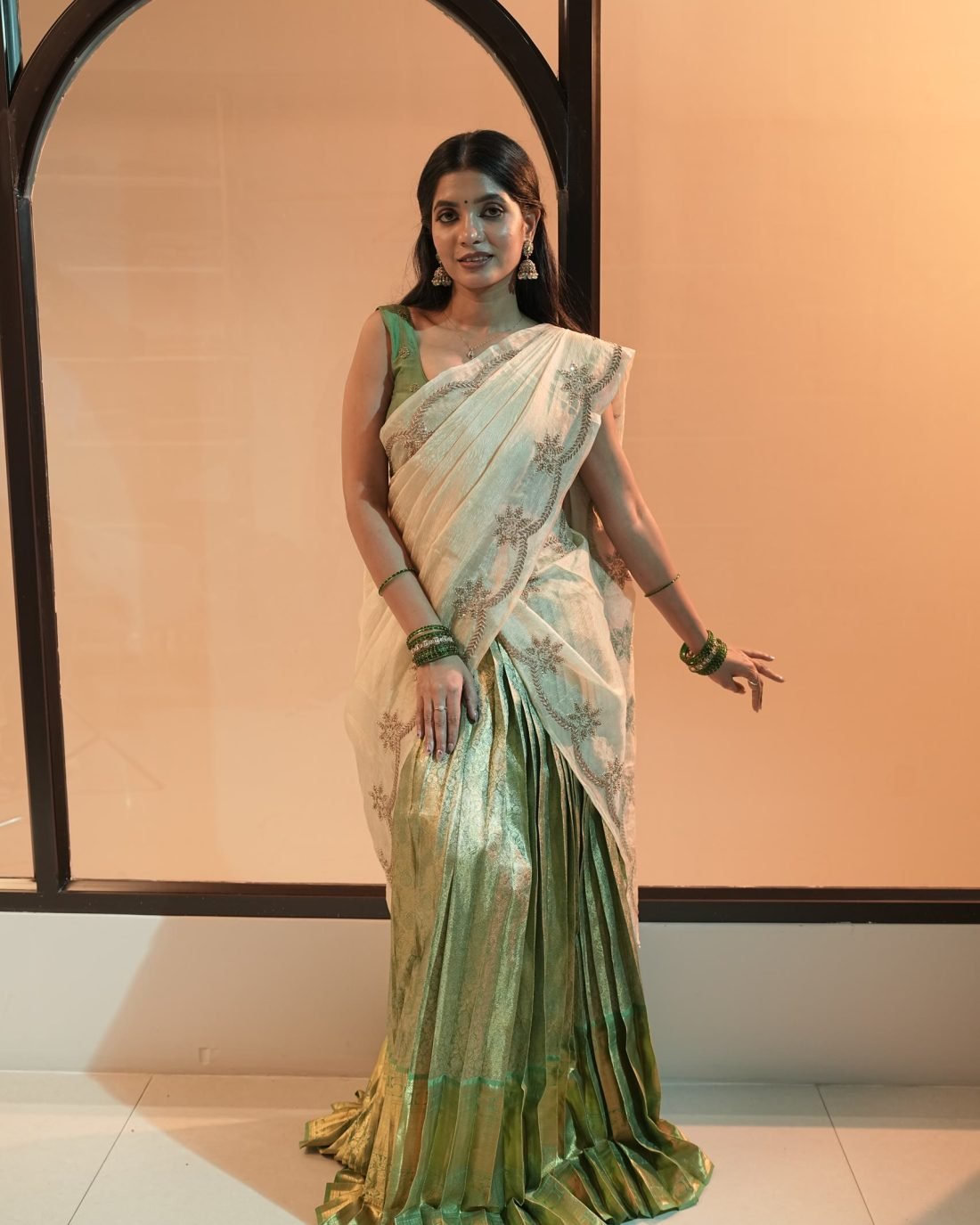 A model in a mint and green saree standing before a pale arched doorway.